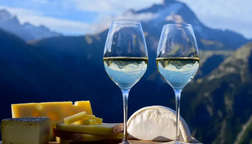 Deux verres de vin blanc avec des fromages devant des montagnes bleues.