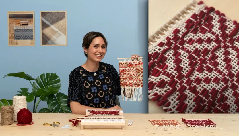 Artisanat textile : une femme souriante tient une petite tapisserie colorée. Sur la table, du fil, des ciseaux et un métier à tisser.