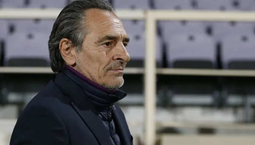 Prandelli, zamyślony trener, w ciemnej kurtce i marynarce, z fioletowym kołnierzem, na tle pustych trybun.