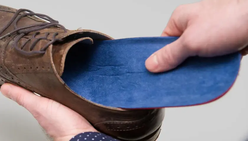 Braune Lederschuhe mit blauen Innenschuhen. Eine Hand hält die Einlage, die andere den Schuh.