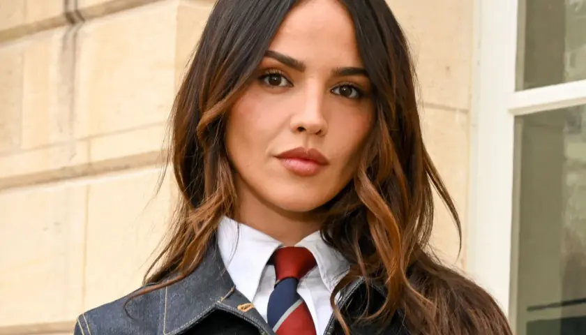 Mujer con cabello castaño y mechas woodlights, viste camisa blanca, corbata y chaqueta vaquera.