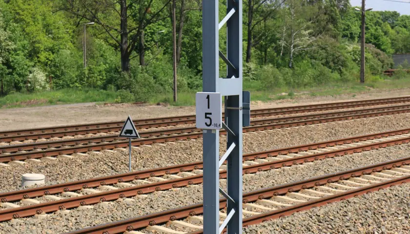 Słup z tabliczką 15-16,4, czyli hektometr kolejowy, obok torów kolejowych.