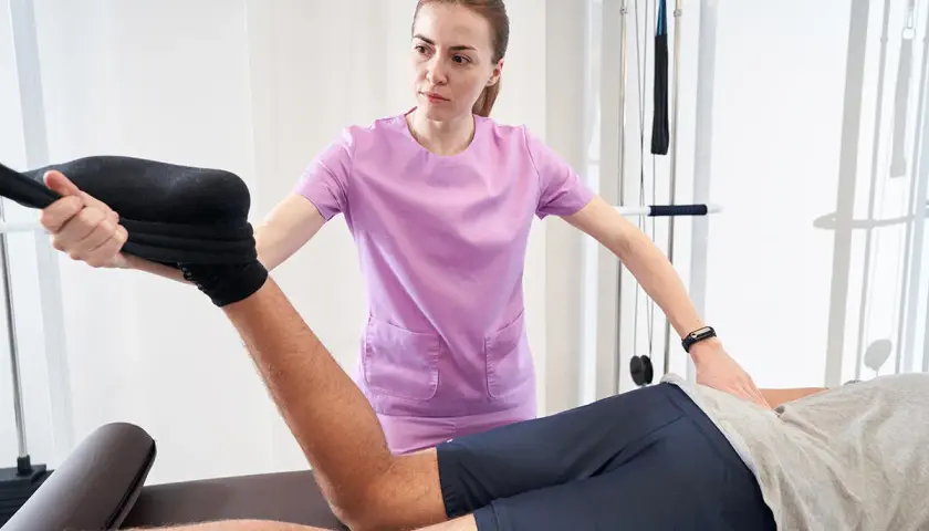Fizjoterapeutka wykonuje test Mennella, pomagając pacjentowi w rehabilitacji kończyny dolnej.