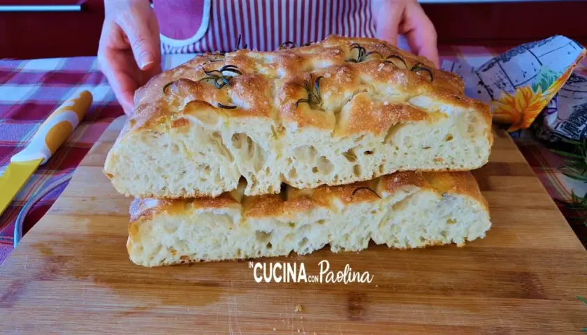 Focaccia alta e soffice, tagliata a metà, con rosmarino e sale grosso. La mollica alveolata promette un sapore delizioso.