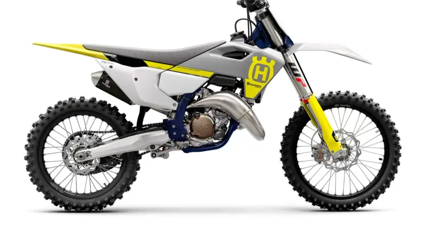 Motocykl crossowy Husqvarna TC125 w kolorze białym z żółtymi i niebieskimi akcentami, gotowy do wyścigów.