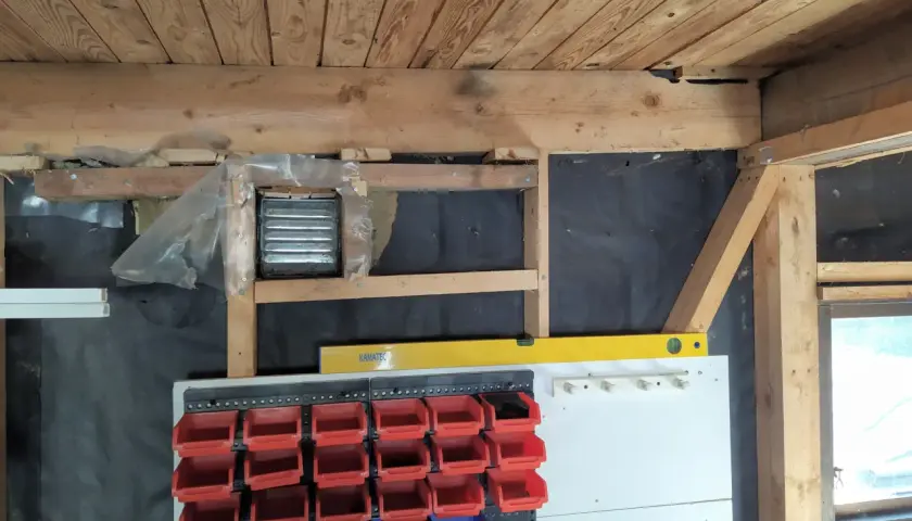 Pågår arbete för att isolera garage. Syns träbjälkar, isolering och förvaringssystem med fack.