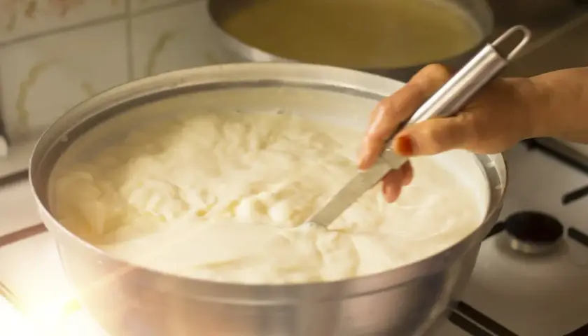 Mano che mescola un pentolone pieno di cremoso yogurt da bere fatto in casa, pronto per essere gustato.