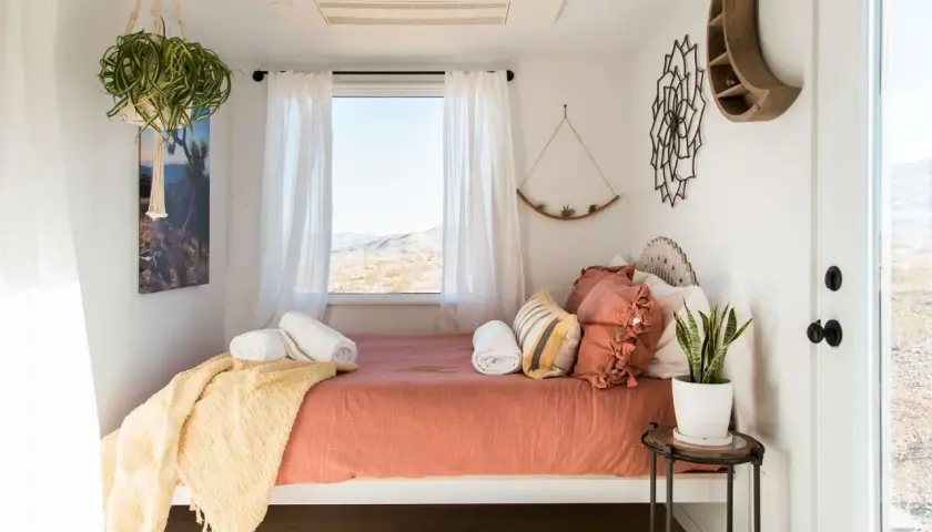 Cozy small bedroom layout with a bed, window view, hanging plants, and desert-inspired decor.