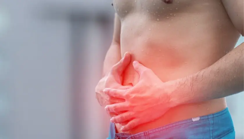 Homme tenant son ventre douloureux, cherchant comment calmer les douleurs d'estomac. La zone rouge indique la douleur.