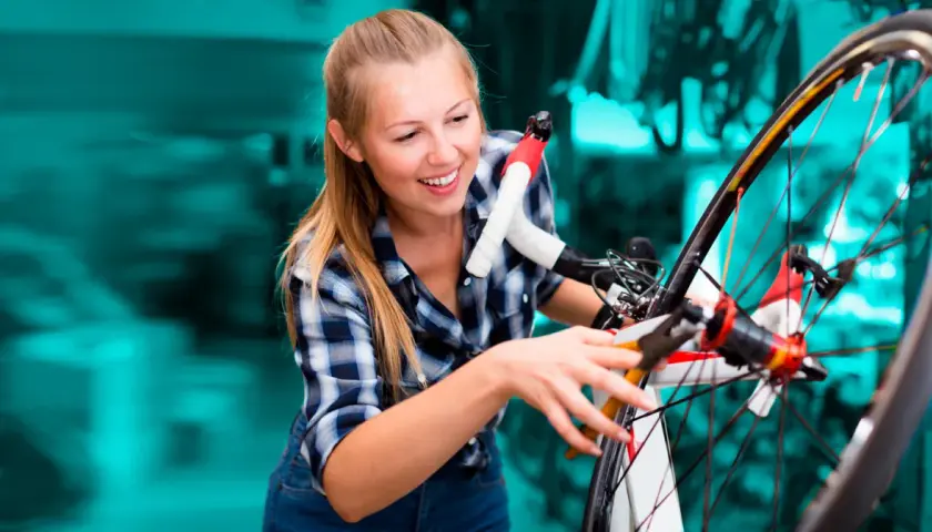 Uśmiechnięta dziewczyna zajmuje się konserwacją roweru, przyglądając się uważnie jego elementom.
