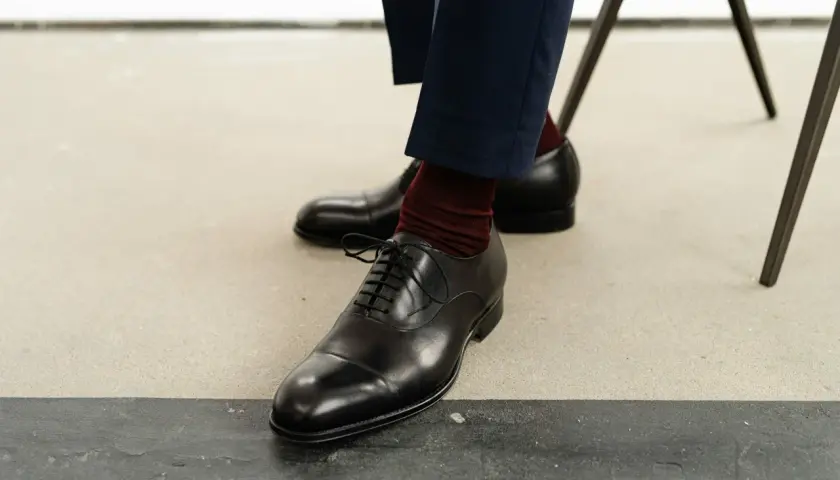 Eleganckie oksfordy, jedne z klasycznych rodzajów butów męskich, w połączeniu z bordowymi skarpetkami i granatowymi spodniami.