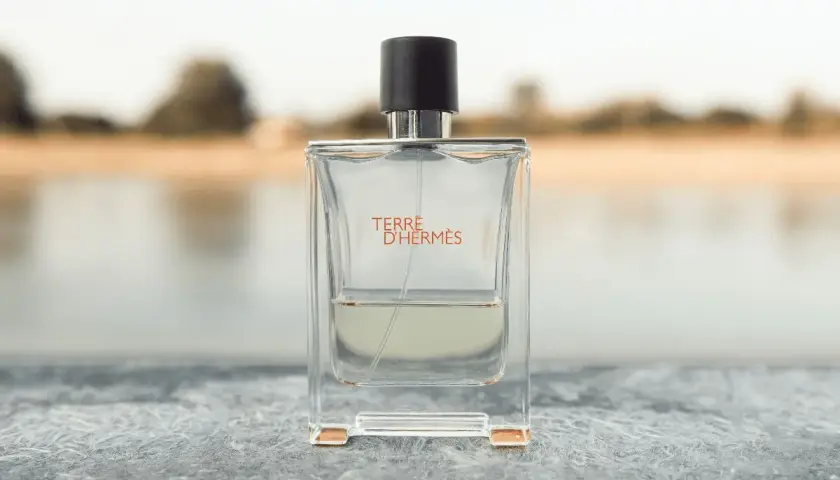 Terre d'Hermès Parfümflasche mit schwarzem Deckel auf Stein, unscharfer Hintergrund.