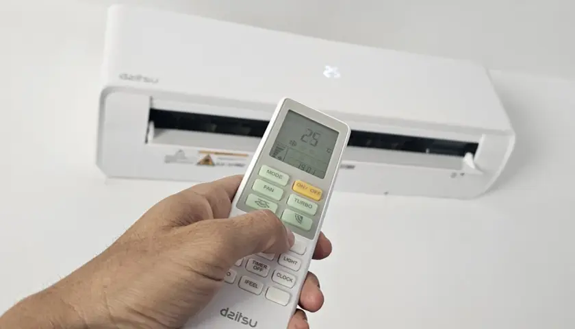 Mano ajustando el control remoto de un aire acondicionado Daitsu. Para poner el aire acondicionado en invierno, selecciona el modo "Calor" o "Heat" en el control.