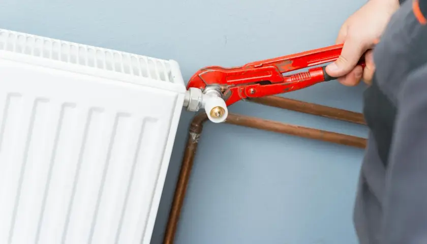 Un idraulico usa una chiave per regolare il raccordo di un termosifone bianco, mostrando come si misura interasse termosifoni per un'installazione corretta.