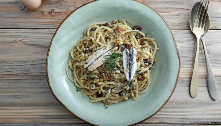Assiette de pâtes au poisson italienne, garnie d'anchois, de pignons de pin et de raisins secs.