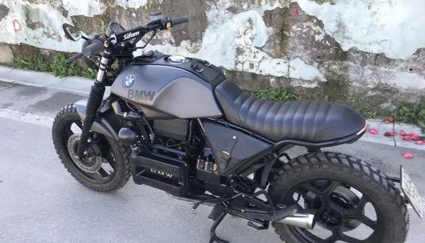 Moto BMW customizzata in stile cafe racer, con serbatoio grigio opaco, sella nera e borse moto laterali in pelle.
