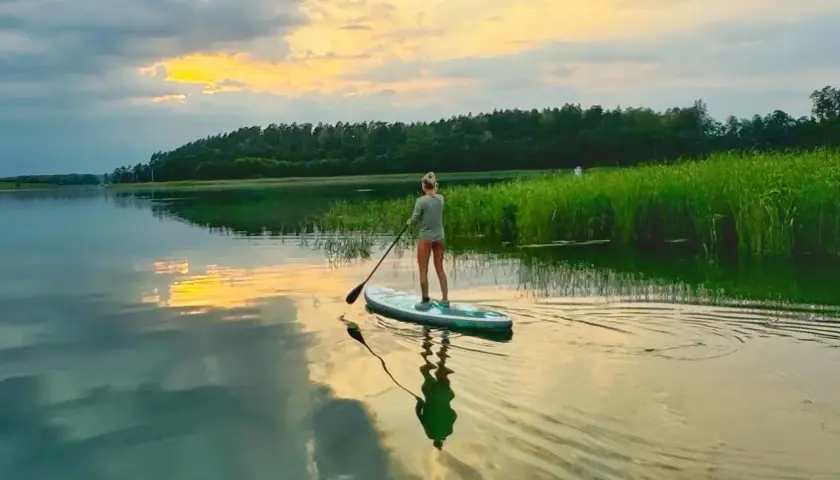 Kobieta na desce SUP, ciesząca się zachodem słońca nad jeziorem. Idealny czas na relaks, może nawet w okolicach Bożego Ciała.