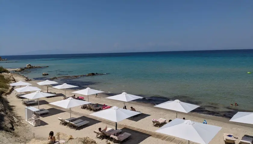 Traumhafter Karibik-Strand auf Chalkidiki mit weißen Sonnenschirmen und Liegen am türkisfarbenen Meer.