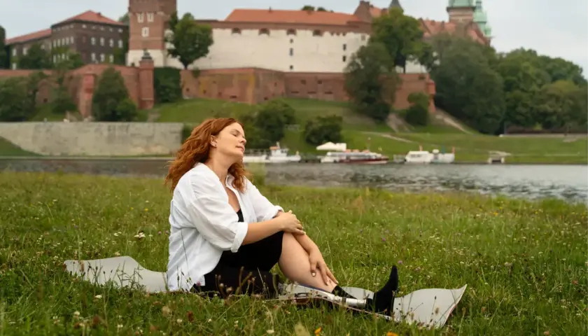Kobieta z rudymi włosami odpoczywa na trawie z widokiem na Wawel. Idealne miejsce na jednodniowe wycieczki z Krakowa.