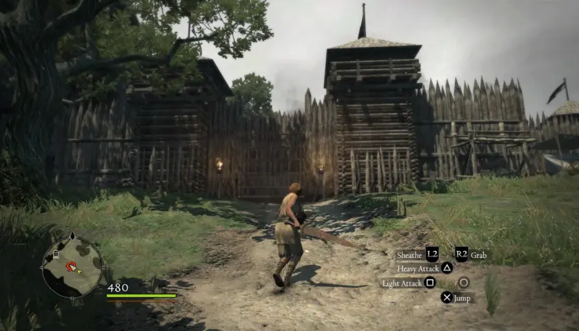 Postać w grze Dragon's Dogma 1 zbliża się do drewnianej bramy warownej.