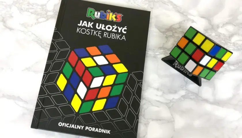 Książka "Jak ułożyć kostkę Rubika" i kostka Rubika na podstawce.