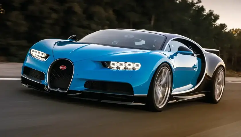 Niebieski Bugatti Chiron pędzi po drodze. Jego cena jest astronomiczna, ale wrażenia z jazdy bezcenne.