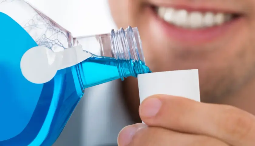 Un uomo versa colluttorio blu in un tappo, un gesto di cura dopo l'estrazione di un dente.