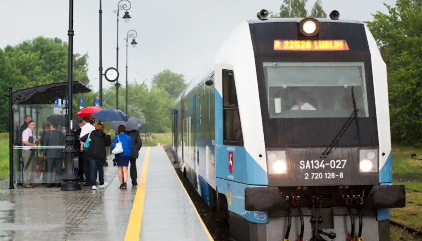 Szynobus Lublin - Zamość trasa. Pasażerowie z parasolami czekają na deszczowy dzień na peronie.