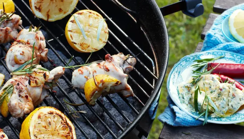 Grillad kyckling med citron och rosmarin på grillen. En tallrik med kyckling, chilifrukter och örtsås står bredvid.