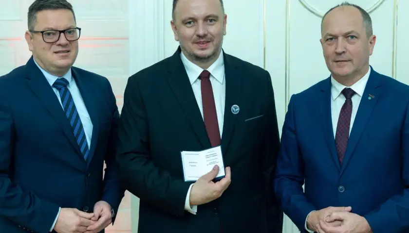 Trzech mężczyzn w garniturach. Środkowy, zasłużony dla kolejnictwa, trzyma certyfikat.