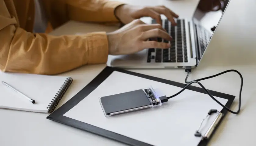 Un homme tape sur son ordinateur portable, un disque SSD externe est branché.