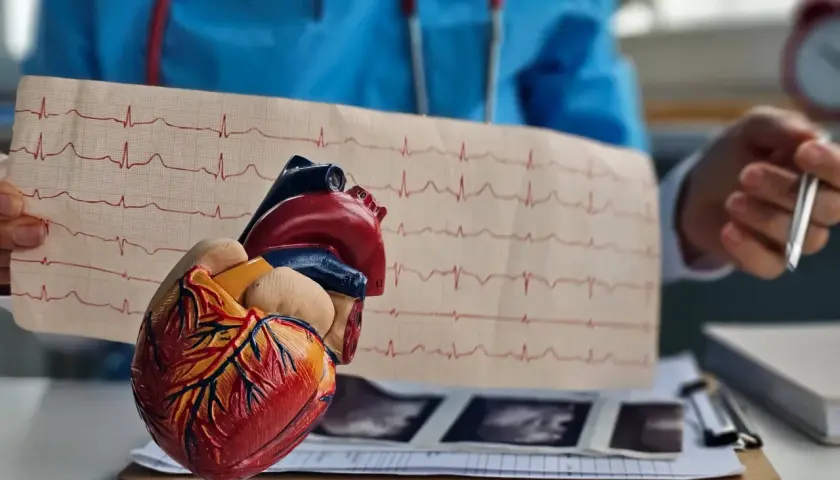 Model serca i EKG na stole lekarskim. W tle lekarz w niebieskim fartuchu, stetoskop i dokumentacja medyczna. To obrazuje pracę z biosotal.