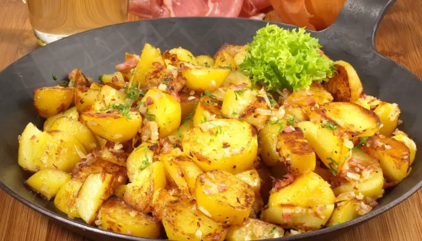 Goldbraune Bratkartoffeln mit Speck und Zwiebeln, garniert mit Petersilie. Ein klassisches Bratkartoffeln Rezept, serviert in einer Eisenpfanne.