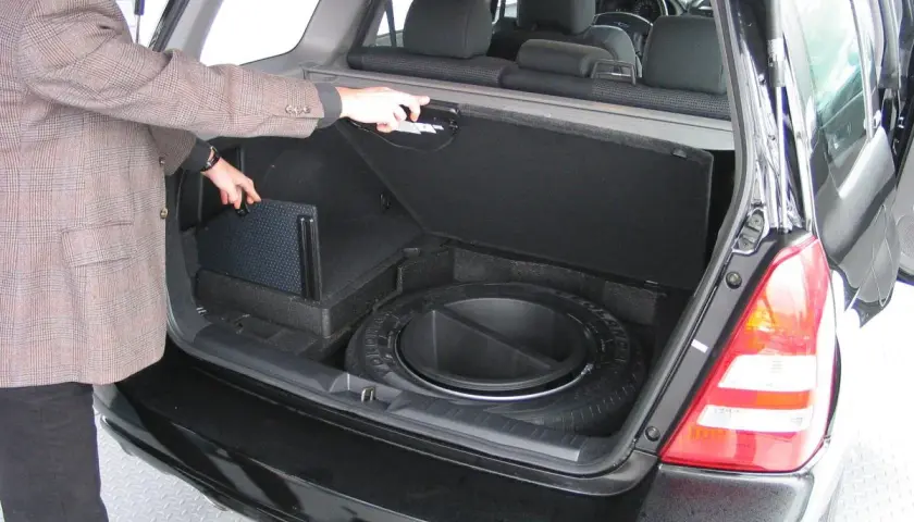 Mężczyzna otwiera bagażnik, pokazując schowek na koło zapasowe i subwoofer. Awaryjne otwieranie bagażnika może być konieczne w razie problemów.