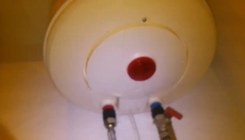 Spód bojlera z podłączonymi wężami i czerwonym wskaźnikiem.