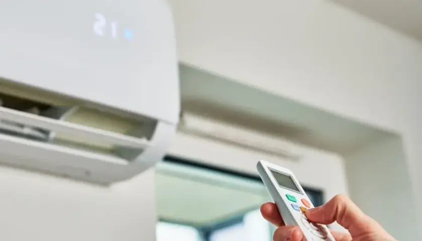 Mano ajustando el aire acondicionado con el control remoto. El símbolo del árbol en el control indica modo ecológico.