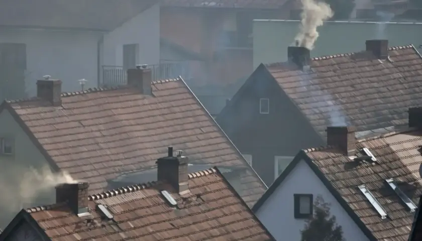 Dym wydobywający się z kominów domów na tle osiedla.