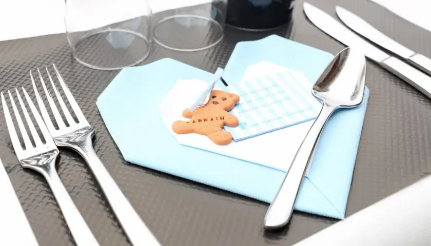 Un biscuit en forme d'ours sur une serviette bleue, prêt pour un baptême. Le tableau budget baptême est bien organisé.