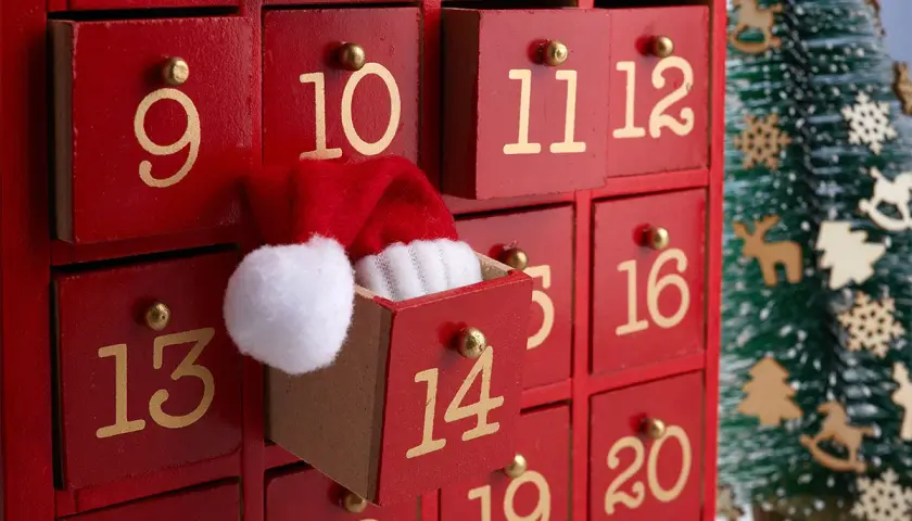 Un calendario dell'Avvento rosso con cassetti numerati. Il cassetto 11 è aperto, mostrando un cappellino di Babbo Natale. Ideale per idee su cosa mettere nel calendario avvento.