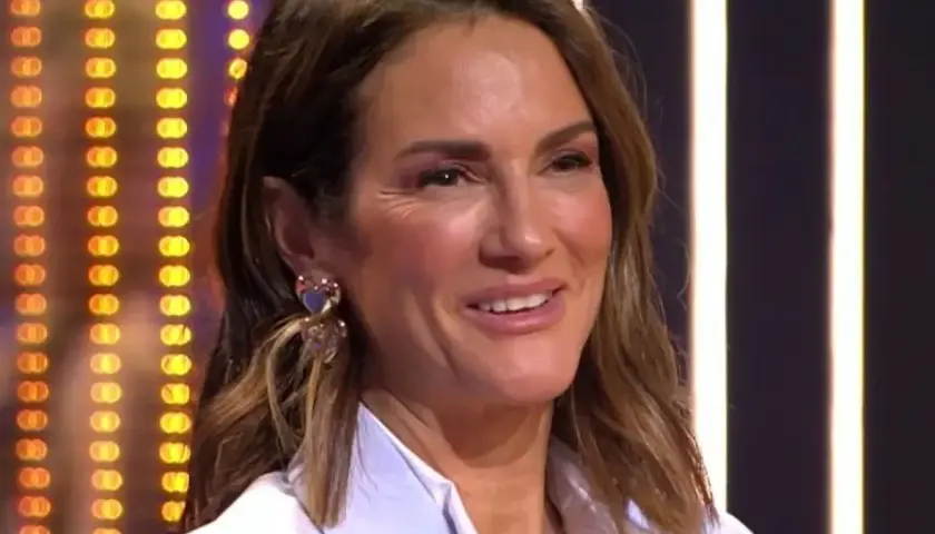 Elena, madre de Adara, sonríe con pendientes de corazón. Fondo de luces.