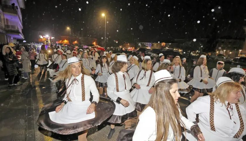 Desfile de mujeres con trajes blancos y sombreros en el carnaval cabezon de la sal, bajo una noche lluviosa.