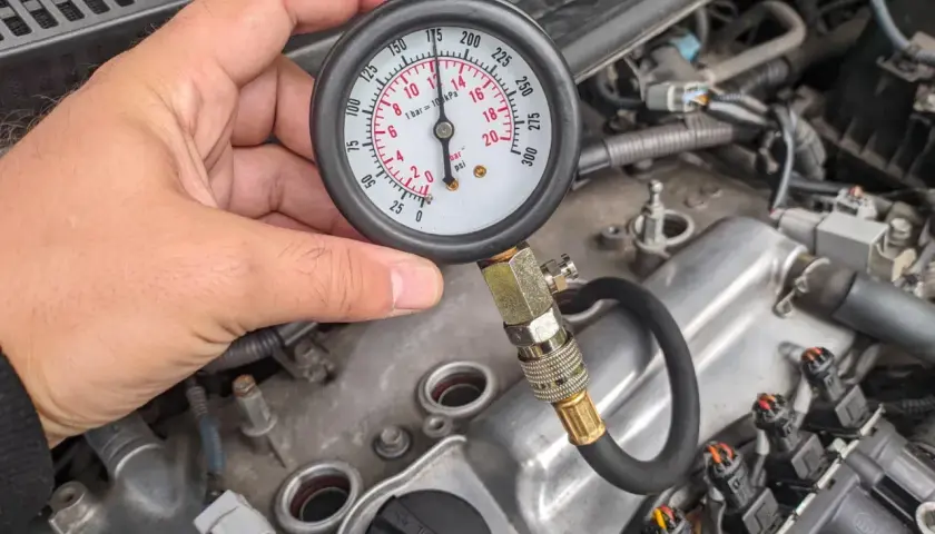 Mężczyzna sprawdza kompresję silnika za pomocą manometru. Wskaźnik pokazuje ok. 170 psi.