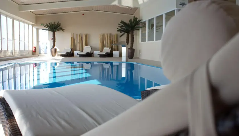 Relaks przy basenie w hotelu Radisson Blu Cottbus. Leżaki czekają na gości obok błękitnej wody i palm.