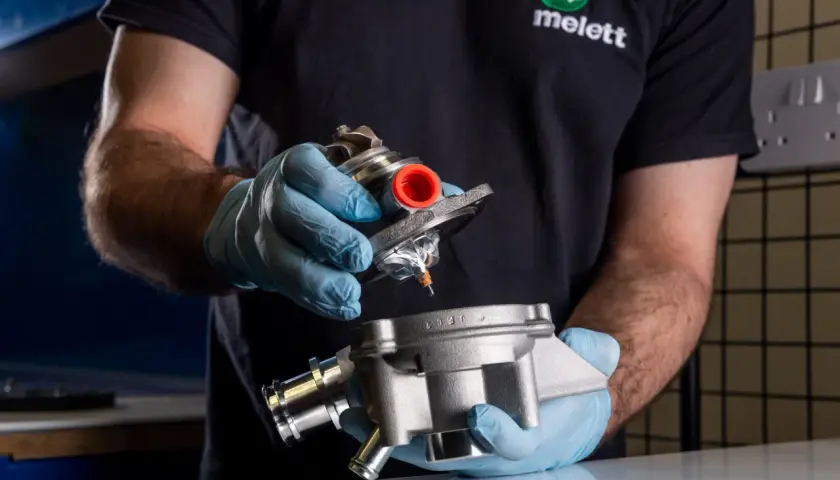Mano con guante azul sostiene un turbo y su carcasa, inspeccionando posible perdida de aceite por el turbo.