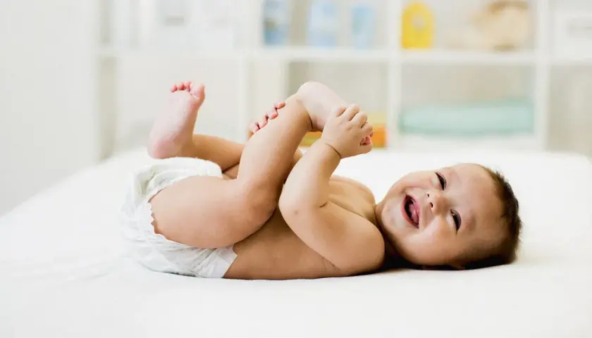 Bambino sorridente in pannolino gioca con i piedini, felice dopo aver fatto la cacca neonato.