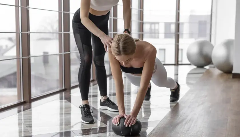 Trenerka pomaga w ćwiczeniu pompki z piłką. Zastanawiasz się, ile cardio w tygodniu jest optymalne?