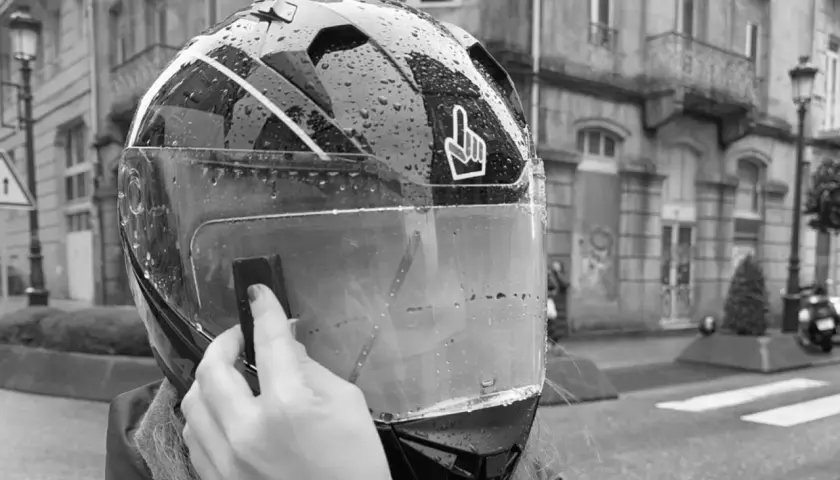 Mano colocando el Pinlock en un casco de moto mojado por la lluvia, listo para instalar.