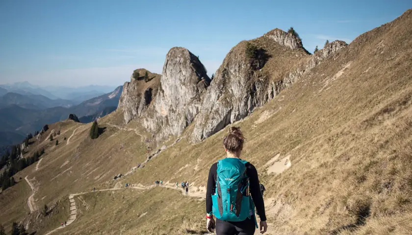 Wanderin auf einem Pfad in den beeindruckenden Berge in Bayern. Die Sonne scheint, der Himmel ist blau.