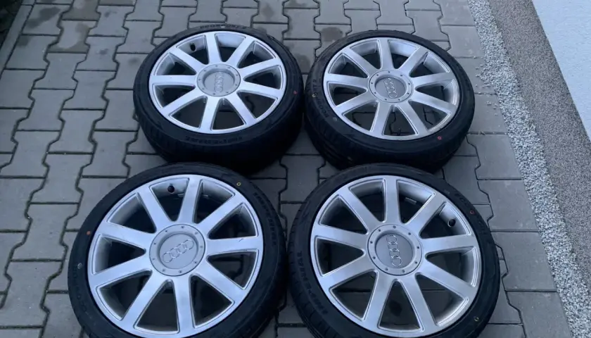 Cztery felgi aluminiowe z oponami do Audi A2. Rozmiar opon widoczny na jednej z nich to 205/55 R16.