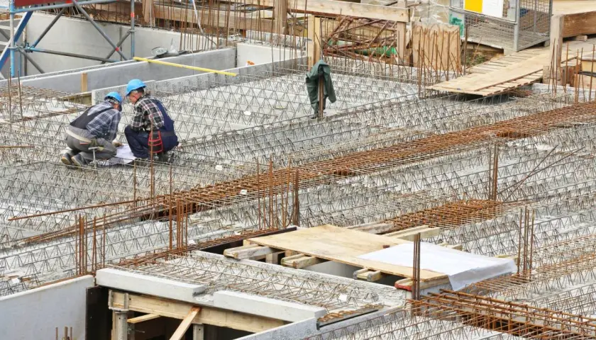 Bauarbeiter prüfen Pläne für verschiedene betondecken arten. Stahlbewehrung für eine massive Betonplatte ist sichtbar.